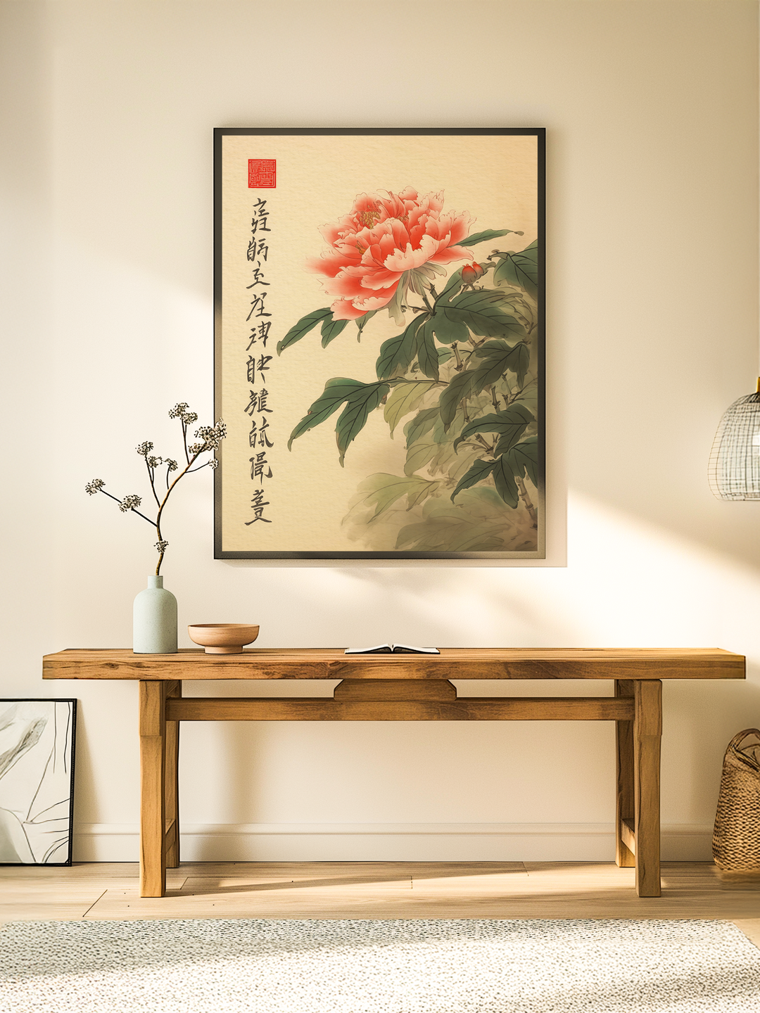 A traditional Asian-style poster with red peony flowers and calligraphy hangs above a wooden console table in a minimalist room with soft natural light, neutral tones, and simple decor elements like a ceramic vase, open book, and woven basket.