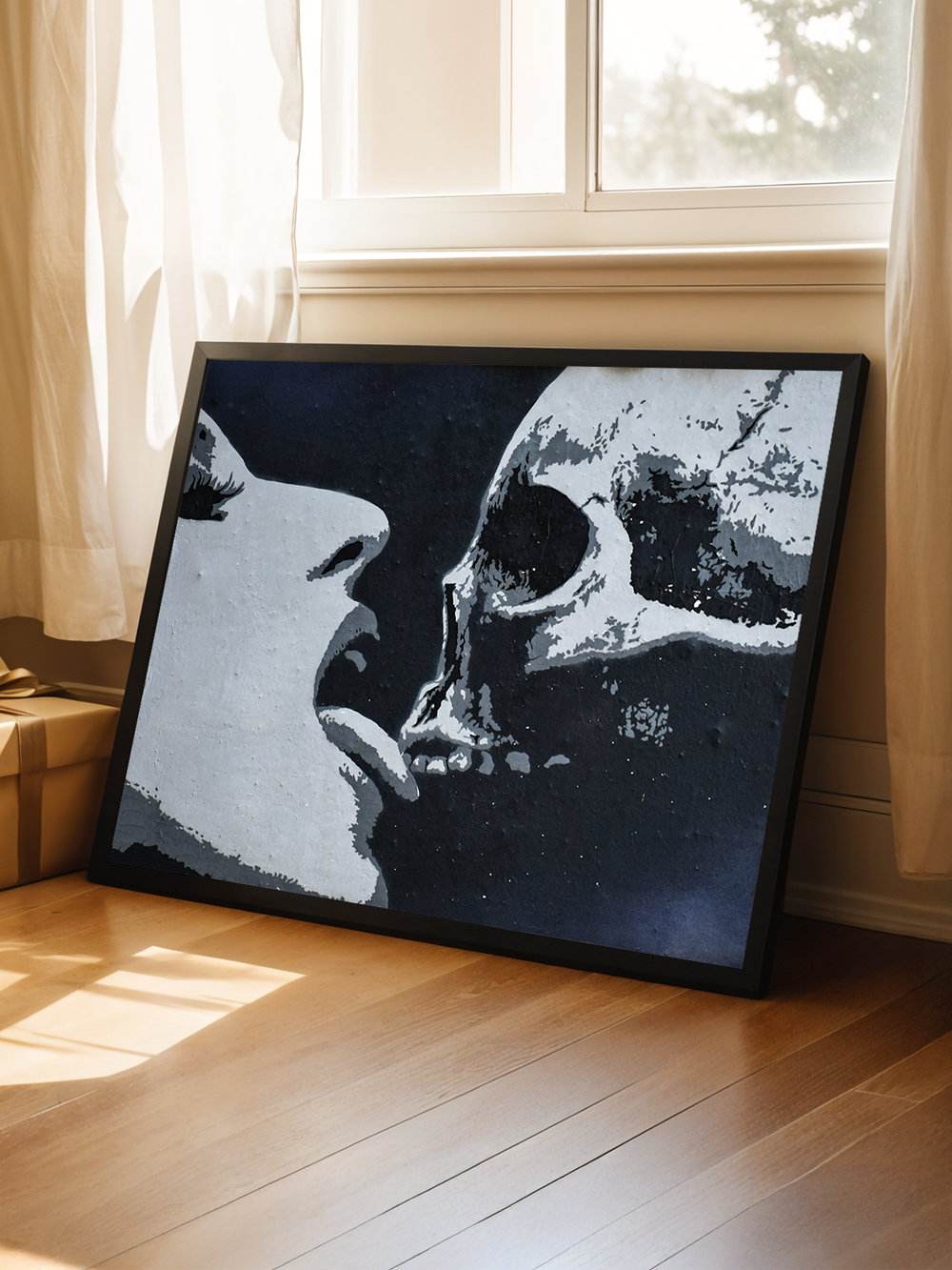 Bold horizontal graffiti-style art print featuring a close-up of a woman facing a skull, symbolizing passion and mortality. The black frame leans casually against a white wall beneath a sunlit window, with soft curtains and wooden flooring creating a contrast between the raw artwork and the warm, natural interior. Ideal for modern apartments and edgy contemporary wall decor.