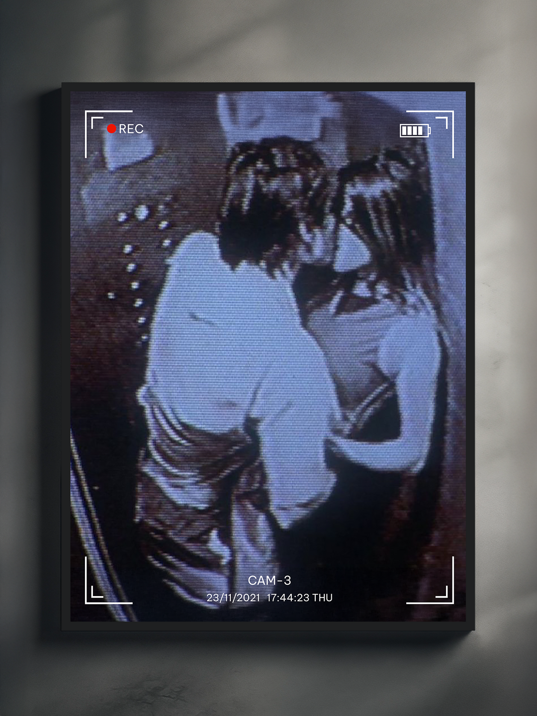 A black-framed poster hanging on a light-colored wall, depicting a grainy black-and-white CCTV recording of a couple kissing in an elevator. The timestamp and overlay graphics give the image a nostalgic, surveillance-themed aesthetic. The poster creates a cinematic and intimate atmosphere.