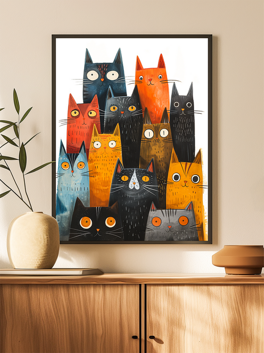 A modern interior scene featuring a framed poster with a whimsical illustration of brightly colored cats, each with unique expressions and wide eyes. The poster is set in a slim black frame and hangs on a light wall above a sleek wooden sideboard. Minimalist decor elements like a ceramic vase, a book, and a sculptural object complete the warm and stylish look of the space.