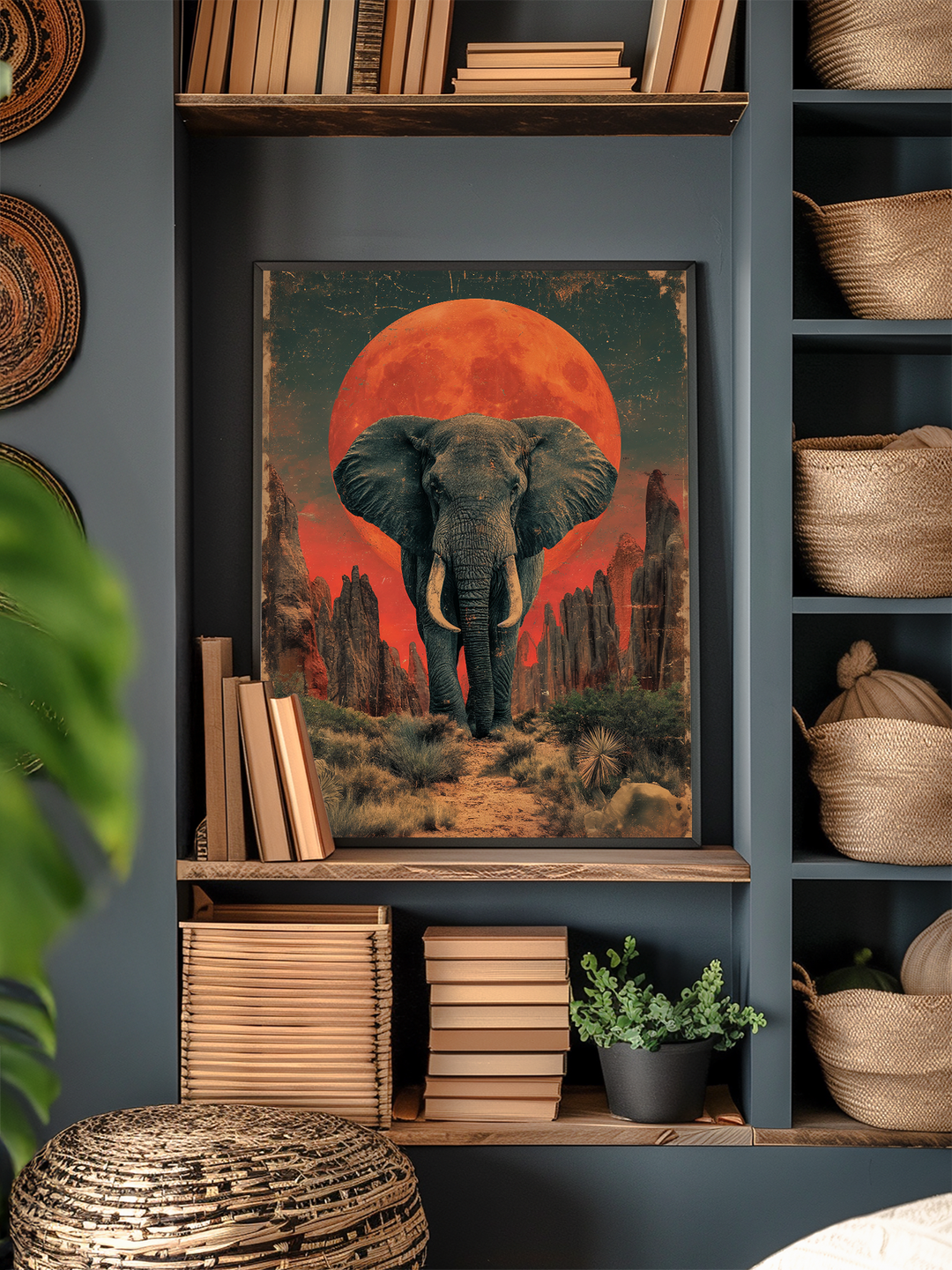 Framed elephant artwork with a vivid red sun and desert landscape set within a modern built-in shelving unit, surrounded by neatly stacked books, woven baskets, a green potted plant, and natural textures that create a warm and inviting interior design aesthetic.