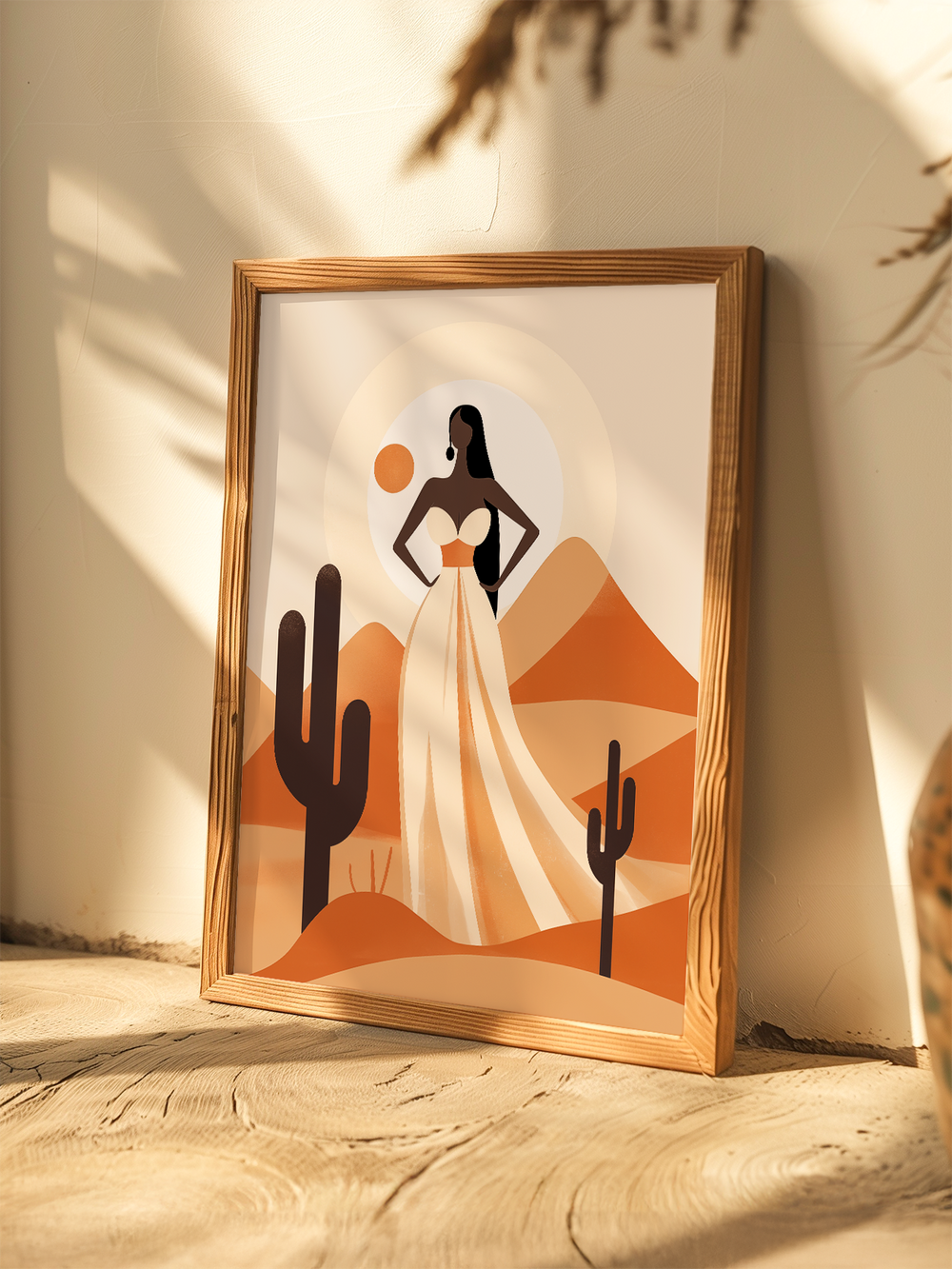 A warm-toned minimalist art print featuring a woman in a flowing white dress standing in a desert landscape with cactus and rolling mountains, displayed in a wooden frame leaning against a light wall with soft sunlight and natural shadows enhancing the earthy ambiance.