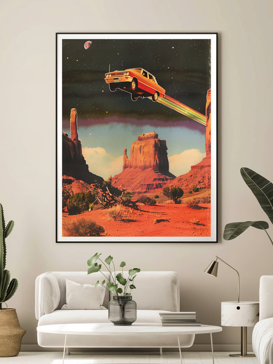 Framed retro poster of a red vintage car flying over desert mesas with rainbow trails, hanging on a light wall above a minimalist white sofa, cactus and plants nearby.