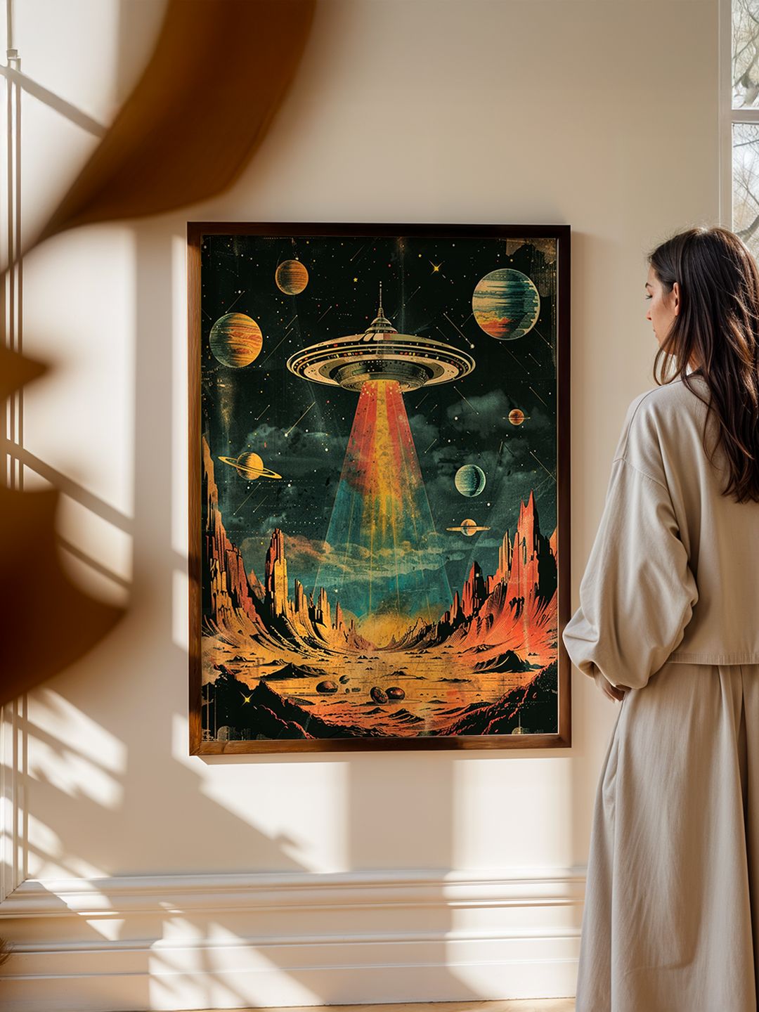 Large framed retro sci-fi poster showing a glowing UFO above an alien desert landscape with colorful planets, displayed on a minimalist wall with a person observing it.