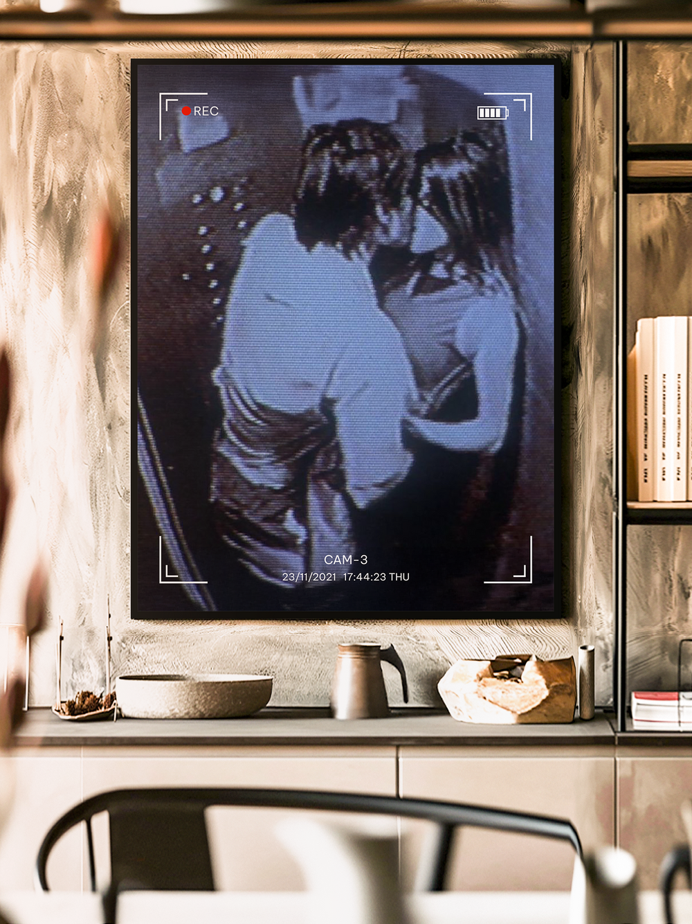 Contemporary art poster depicting a couple sharing a kiss, styled like a grainy CCTV recording with timestamp and camera frame details. The artwork hangs in a modern interior with warm lighting, shelves, and minimalist decor, creating a cinematic and intimate atmosphere.