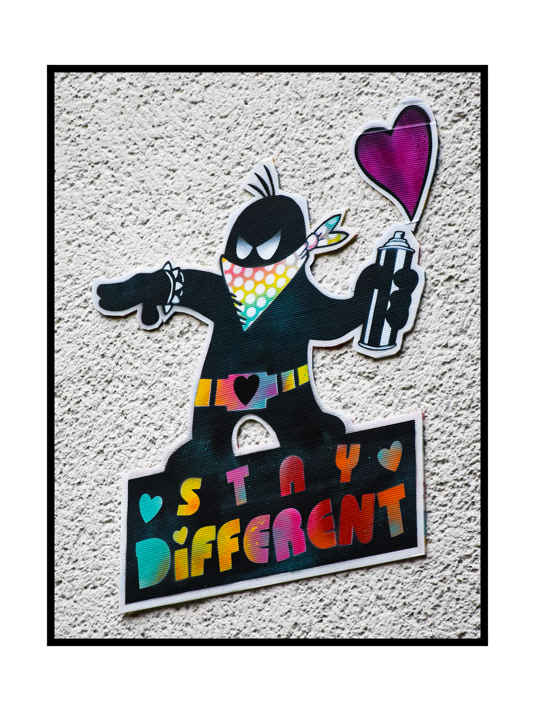 A colorful street art graffiti illustration showing a masked character holding a spray can with a heart symbol, standing above the words “Stay Different.” The artwork uses bold shapes, vibrant colors, and a playful urban style, expressing individuality, creativity, and a positive message rooted in modern graffiti culture.