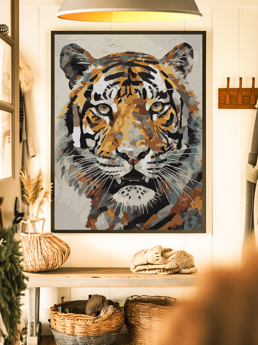 Framed tiger artwork in bold orange, black, and neutral tones displayed on a white textured wall. The print features a close-up of a tiger’s face with a modern, abstract style. It hangs above a wooden console table decorated with woven baskets and natural elements, creating a cozy, rustic atmosphere.
