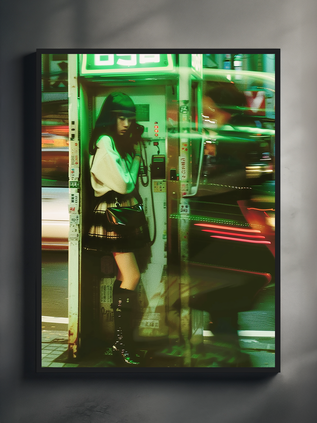 Framed photographic poster showing a girl in a Japanese phone booth at night, surrounded by motion-blurred city traffic and green neon lights, mounted on a light gray wall with soft shadows for a modern and cinematic urban aesthetic.